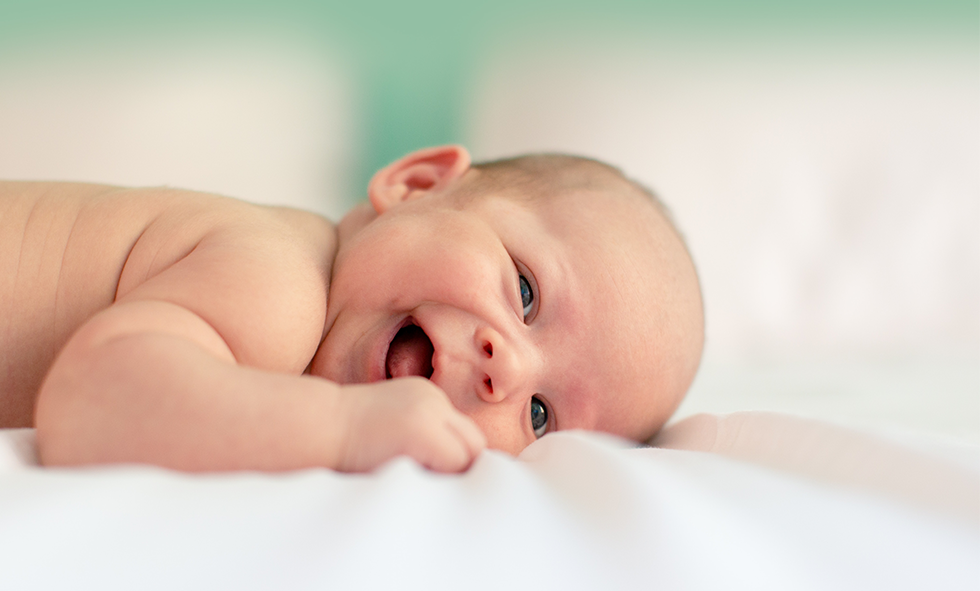 smiling baby laying on white sheets