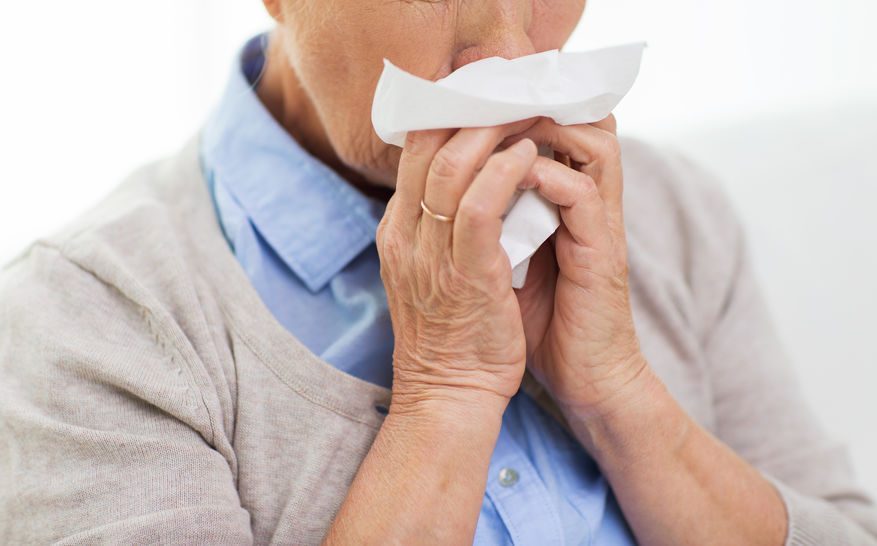 sick senior woman blowing nose to paper napkin