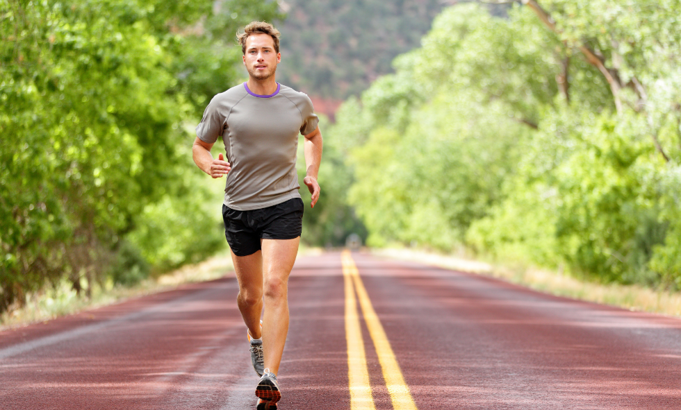 man running on dirt road with green trees in the background men's health
