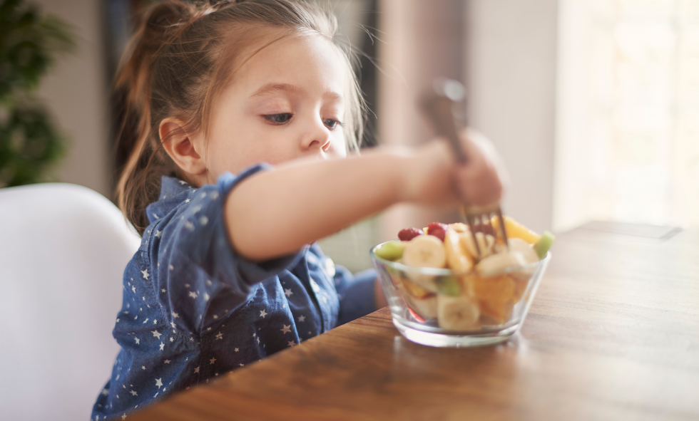 child in blue dress snacking on fruit on the table