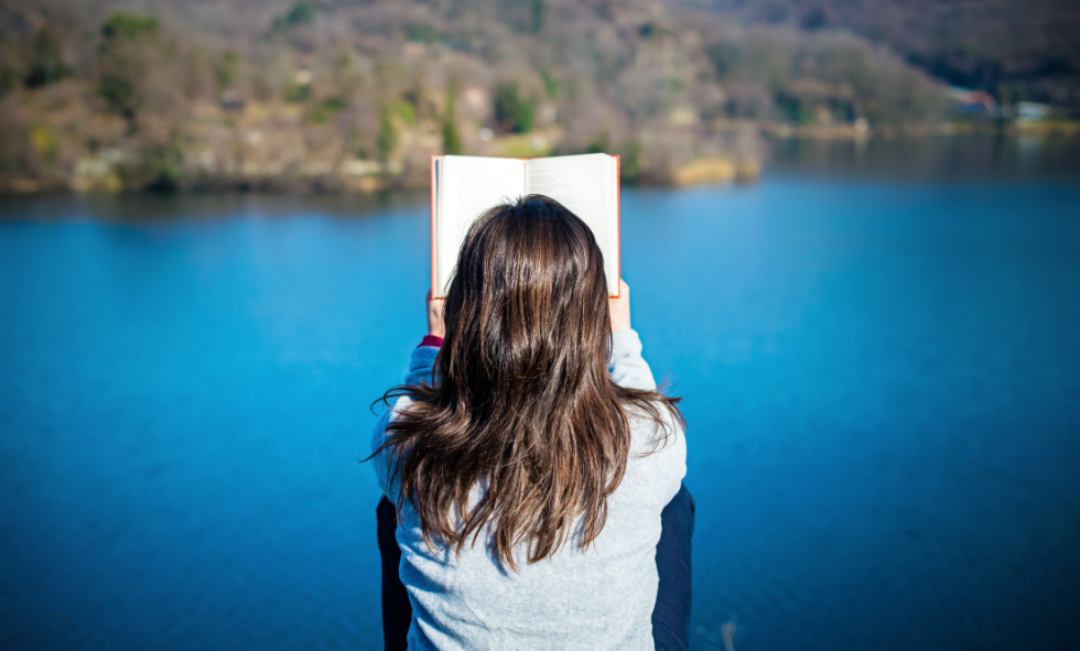 woman with new years resolution to read more sitting in front of lake reading book