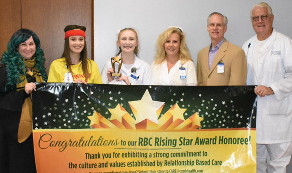 Caitlyn Reser holding award behind Rising Star banner with CCMH Staff