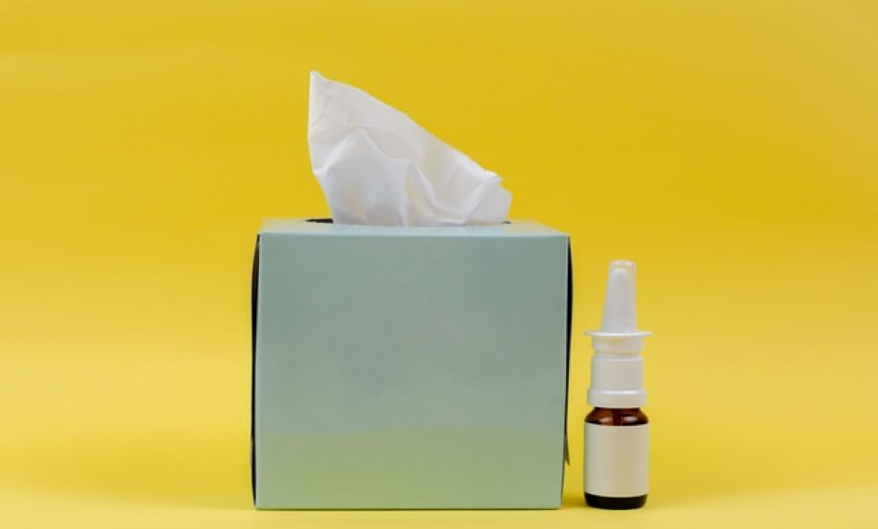 box of tissues and bottle of nasal spray in front of yellow background to alleviate spring allergies