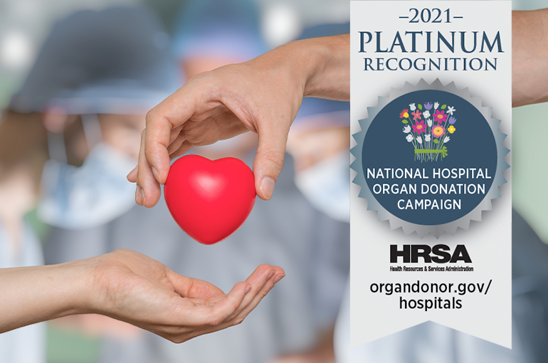 two hands passing a plastic heart to each other, with banner that says "2021 Platinum Recognition National Hospital Organ Donation Campaign"