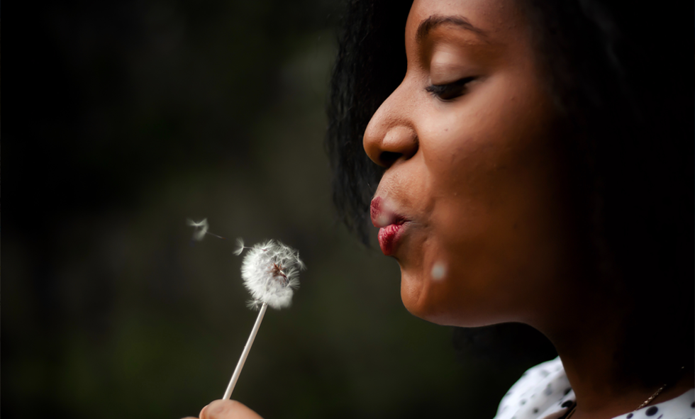 woman blowing dandelion in summer