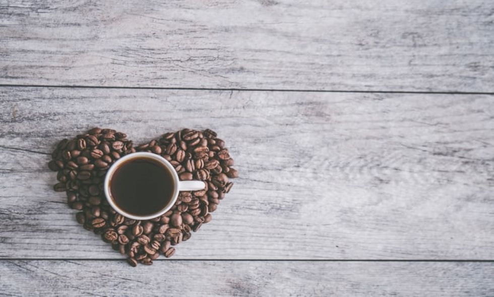 coffee beans shaped into heart with cup of coffee in the middle sitting on a wooden table