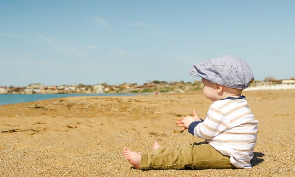 infant sitting at beach with sun protection clothing - sunblock application