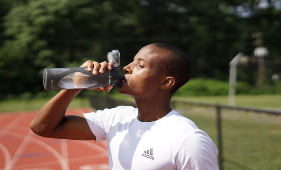 African American man drinking water after exercising outside to avoid dehydration