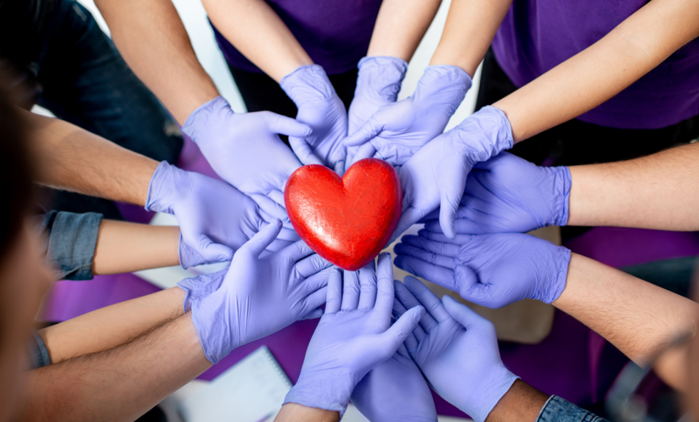 a group of hands all wearing surgical gloves holding a heart